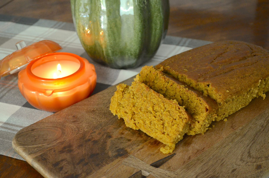 Sliced solar-baked pumpkin bread on a wooden board with a candle and a green pumpkin